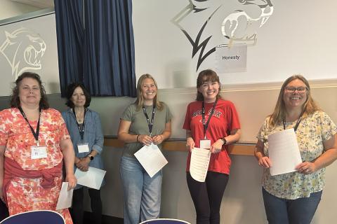 A group of women pose together holding papers for a presentation.