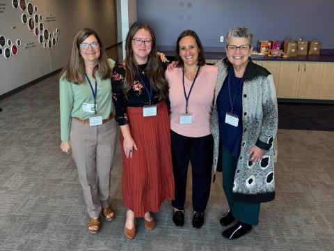 Four women in professional attire standing for a photo at a meeting