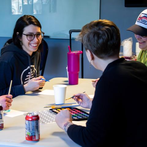 Young adults laugh together at a table while working on painting with watercolors.