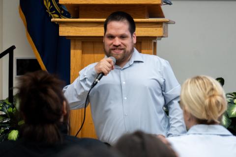 Photo of Tim Houle speaking while holding a microphone. 