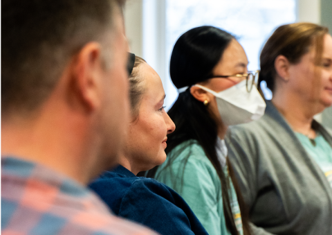 A group of adults in a classroom are looking forward