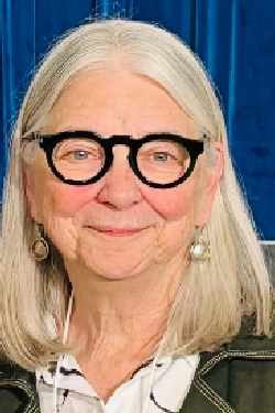 Headshot of Joanne Nicholson smiling, with chin-length hair, wearing glasses and a dark blazer with red top. 