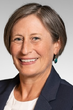 Headshot of Katherine McDonald smiling, with short brown hair, wearing a blazer and light top. 