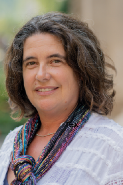 Headshot of Laura Slugg smiling, with chin-length brown hair, wearing a white blouse with multicolor scarf. 