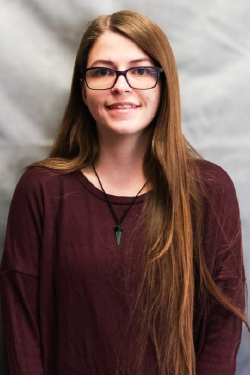 Headshot of Liberty Hicks smiling, with long hair, wearing glasses and a burgundy sweater. 