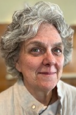 Headshot of Maria Paiewonsky smiling, with short hair, wearing a button up light shirt. 