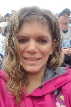 Headshot of Courtney Krueger smiling, with long wavy hair, wearing a pink zip up jacket. 