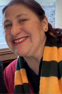 Headshot of Jena Crafton smiling, with brown hair pulled back, wearing earrings and a colorful scarf. 
