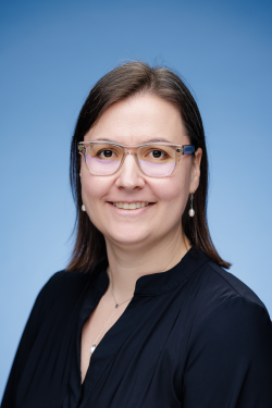 Headshot of Lieke van Heumen smiling, with shoulder-length brown hair, wearing glasses and a black blouse. 
