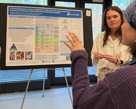Photograph of a scientific research poster presentation titled "A Tiered Approach to Infant Rehabilitation: Addressing Neurodevelopmental Outcomes in Neonatal Opioid Withdrawal Syndrome (NOWS)." Two women discuss the poster 