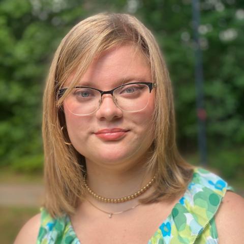 Elizabeth Hull is a blonde woman wearing glasses and a blue and green printed blouse.