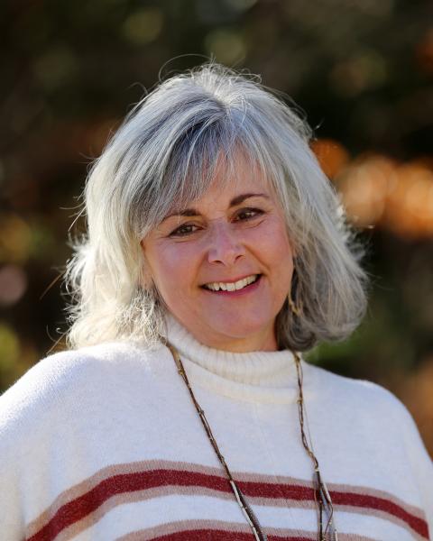 Kathy Francoeur is a woman with shoulder length grey hair wearing a soft white knit sweater with red stripes
