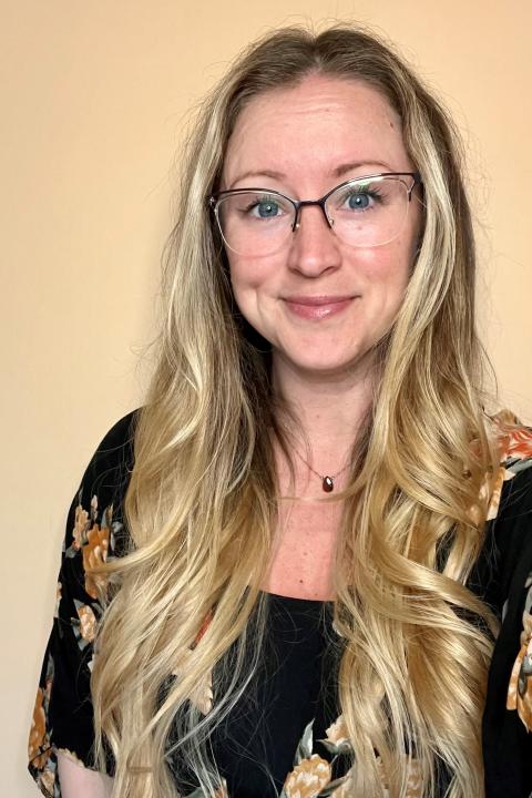 Jennifer Boisvert is a woman with long wavy blond hair wearing glasses and a black blouse with flowers on it