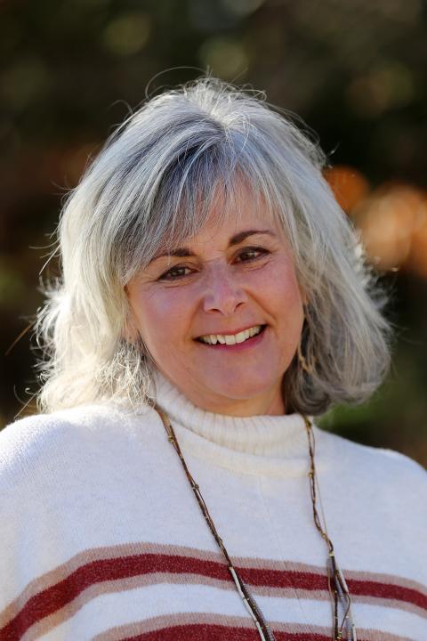 Kathy Francoeur is a woman with shoulder length grey hair wearing a soft white knit sweater with red stripes