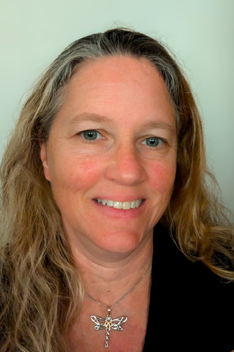 Elaine Wheeler is a woman with wavy light colored hair. She is smiling and wearing a black blouse and silver dragonfly necklace.