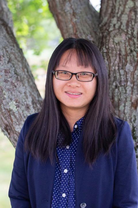 Xueting is a smiling woman with glasses and long black hair standing outside in the shade of a tree.