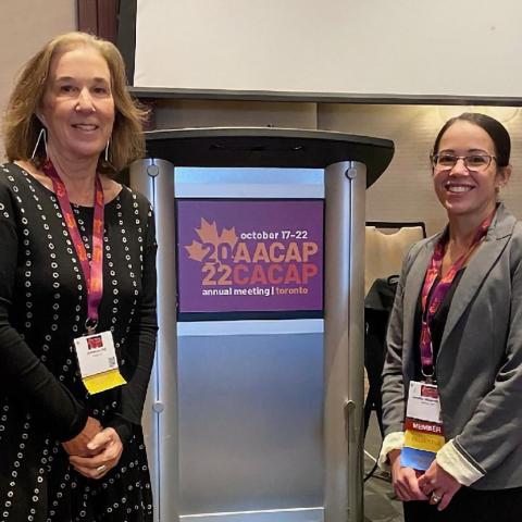 two women stand in front of a podium for the 2022 AACAP/CACAP annual meeting in Toronto