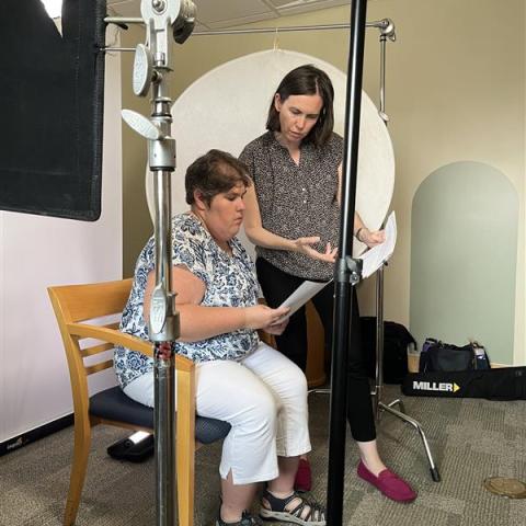 Two women review a script with film equipment around them.