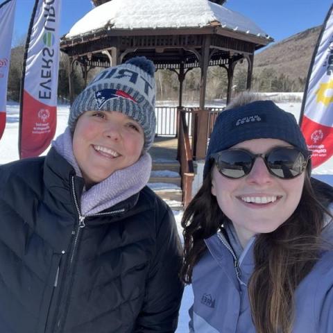     Two women wearing hats and winter coats in front of a snowy, mountain background.  