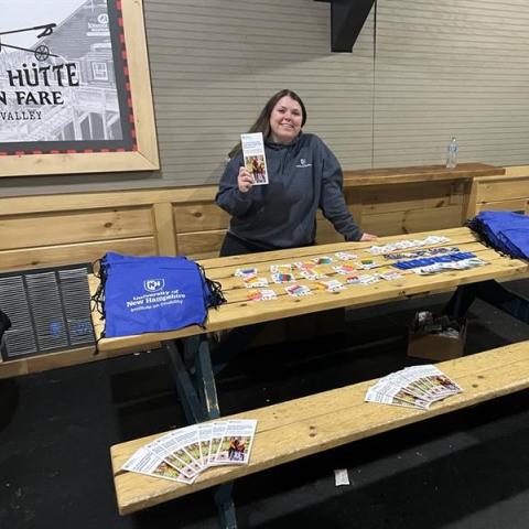 A woman stands behind a table of Health Linkage Program promotional materials.