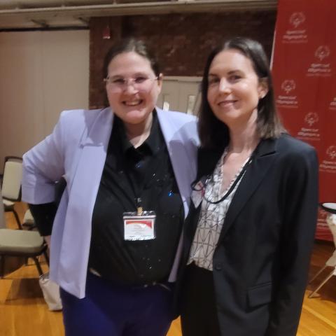 Two individuals wearing blazers pose at an event.  